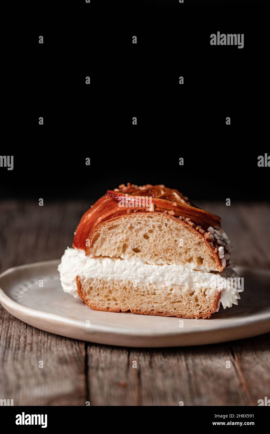 Appetitosa fetta di torta del re farcita con panna bianca sul piatto posto su tavola di legno su sfondo nero Foto Stock