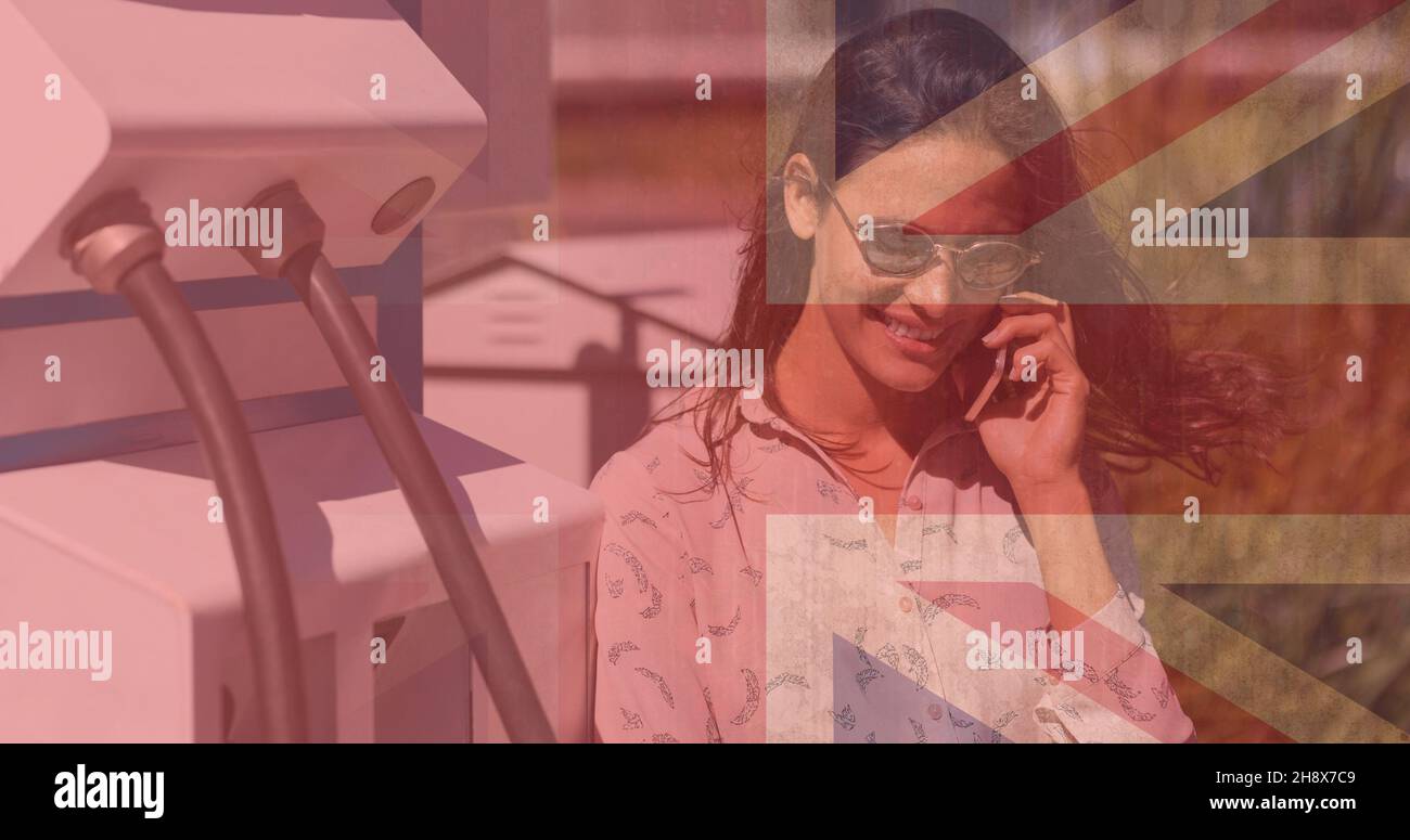 Composito digitale di donna sorridente che parla al telefono alla stazione di ricarica elettrica con jack Union Foto Stock
