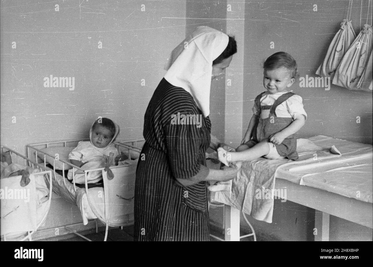 Polska, 1946. Sipialnia dzieci w sierociñcu. NZ. Oppiekunka ubiera jedno z podopiecznych dzieci. Gr PAP/Stanis³aw D¹browiecki Dok³adny miesi¹c i dzieñ wydarzenia nieustalone. Polonia, 1946. Una camera da letto nell'orfanotrofio. Nella foto: Un chaperone vestito un bambino. Gr PAP/Stanislaw Dabrowiecki Foto Stock