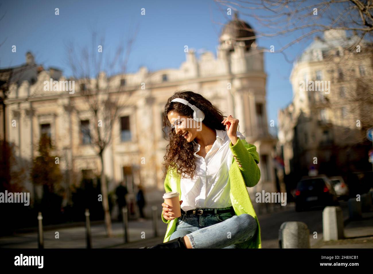 Bella giovane donna che ascolta musica con smartphone in strada e tiene il caffè da asporto Foto Stock