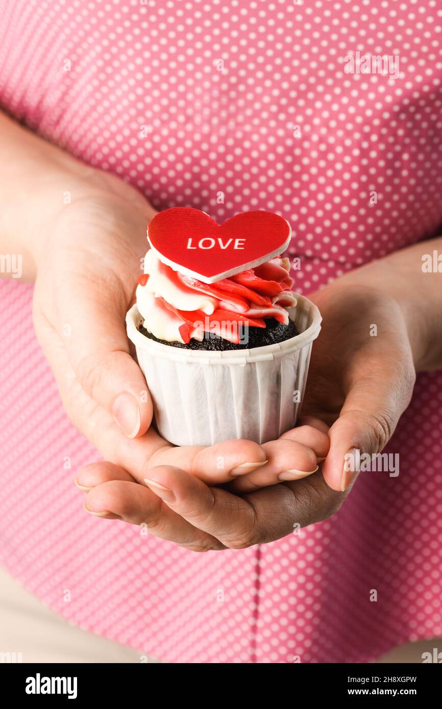 Cuore modellato Cake nelle mani con l'iscrizione Love for San Valentino e 14 febbraio. Cupcake a forma di cuore primo piano Foto Stock