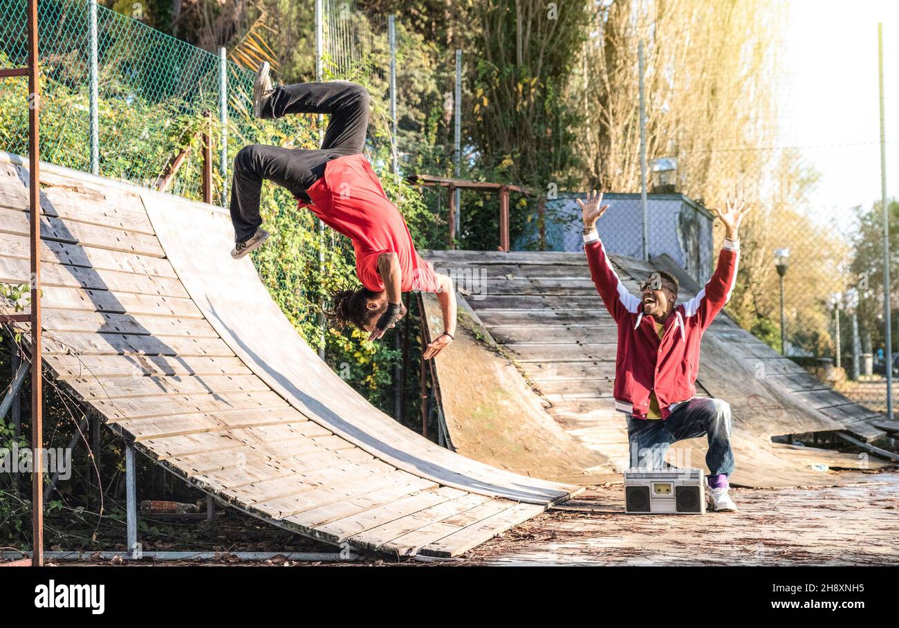 Atleta urbano che esegue salto con il somersault flip al skate Park - ragazzo Afroamericano che guarda l'amico acrobat ballare con estrema flipping move Foto Stock