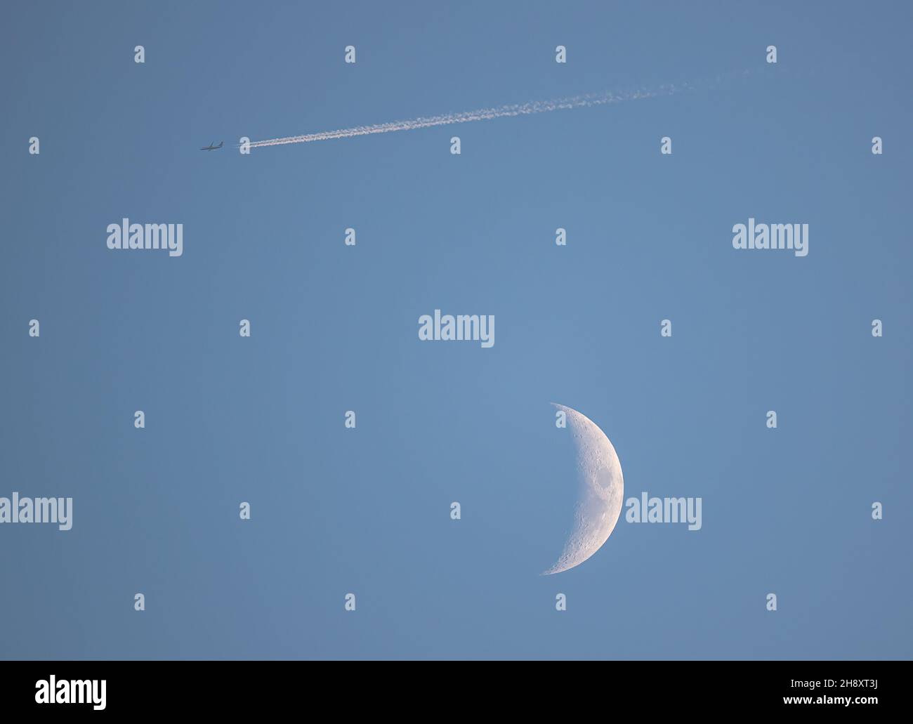 Fly me alla luna o in questo caso oltre esso . Crescent moon, un aereo e un percorso di vapore in cielo azzurro chiaro. Suffolk, Regno Unito Foto Stock