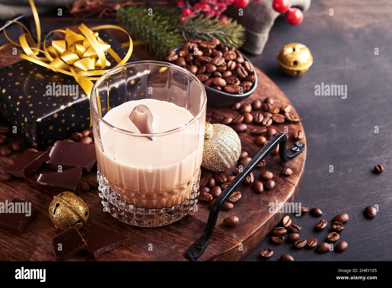 Bicchiere di crema irlandese liquore baileys con ghiaccio, caffè torrefatto in chicchi, cannella, decorazioni natalizie e cioccolato su tavola di fondo in legno scuro. Chris Foto Stock