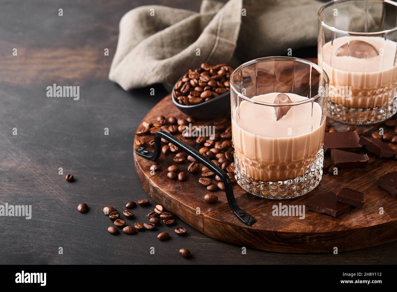 Bicchiere di crema irlandese liquore baileys con caffè torrefatto in chicchi, cannella e cioccolato su tavola di fondo in legno scuro. Messa a fuoco selettiva. Foto Stock