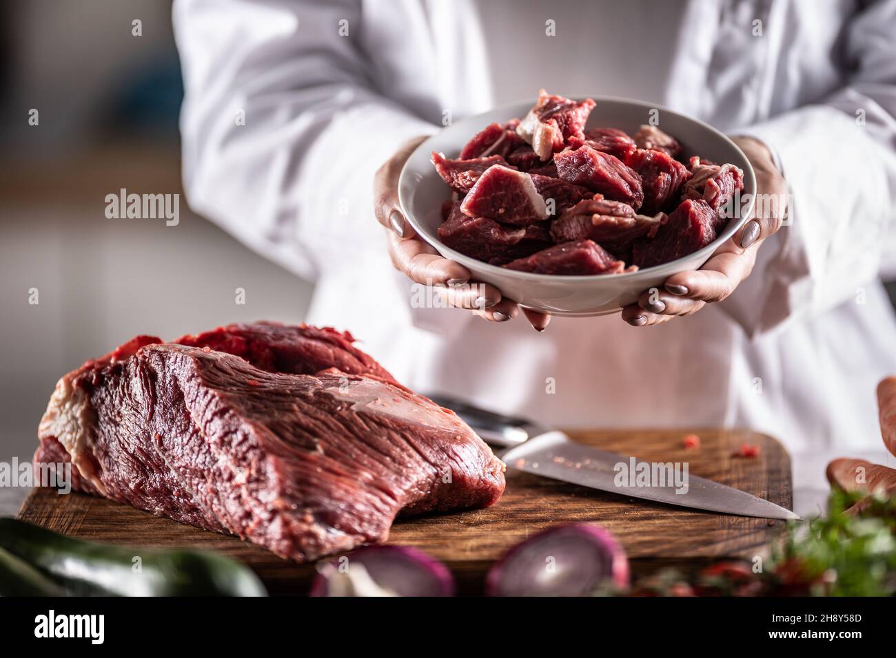 Piccoli pezzi di manzo o maiale da stufato in una ciotola accanto a un grosso pezzo di carne rossa su un tagliere. Foto Stock