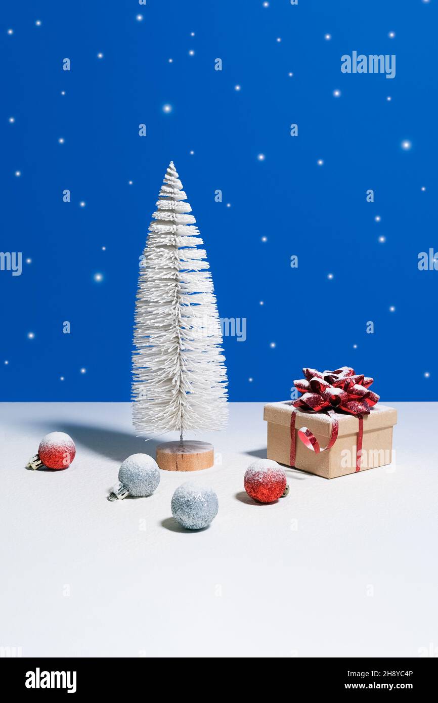 Bella bandiera di Natale o di Capodanno. Albero di Natale giocattolo, scatola regalo con arco rosso e baubles di Natale su sfondo blu con la neve caduta sul Foto Stock