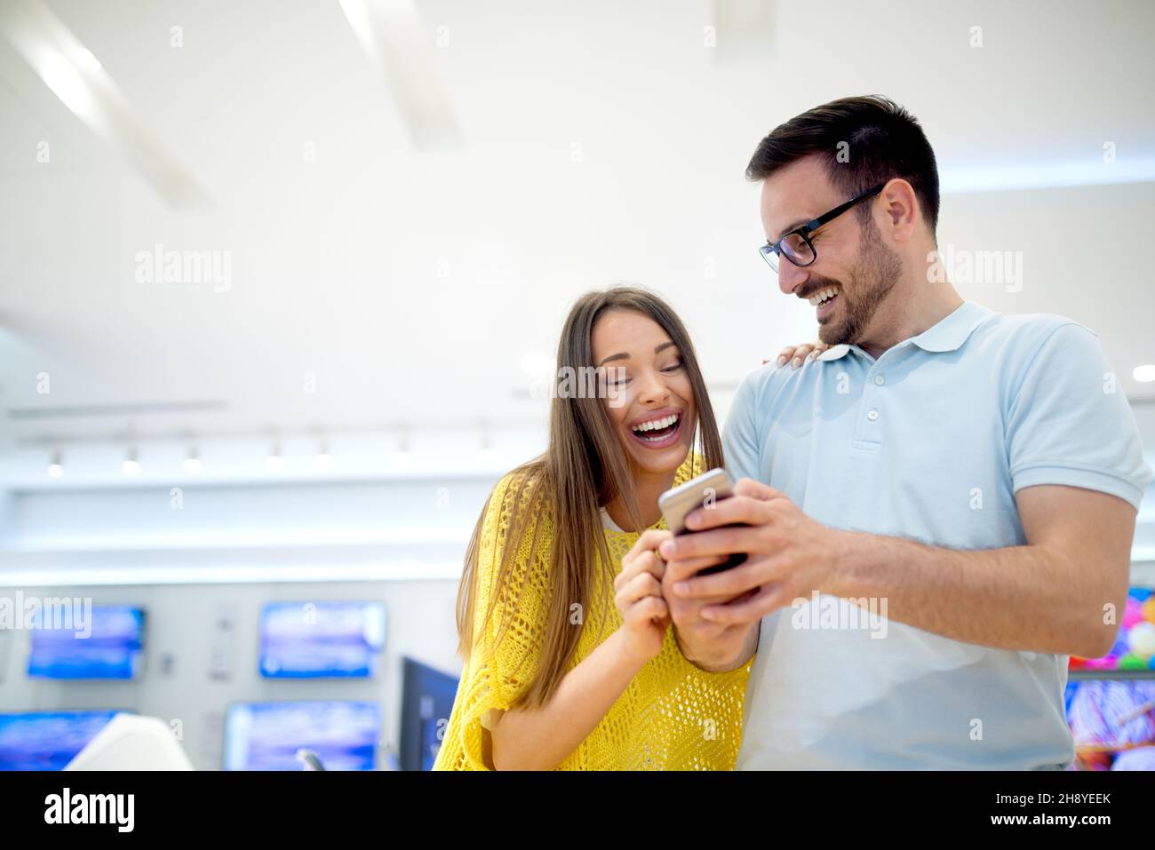 Giovane bella coppia che acquista nuovo telefono cellulare al negozio di tecnologia. Divertitevi a fare shopping. Foto Stock