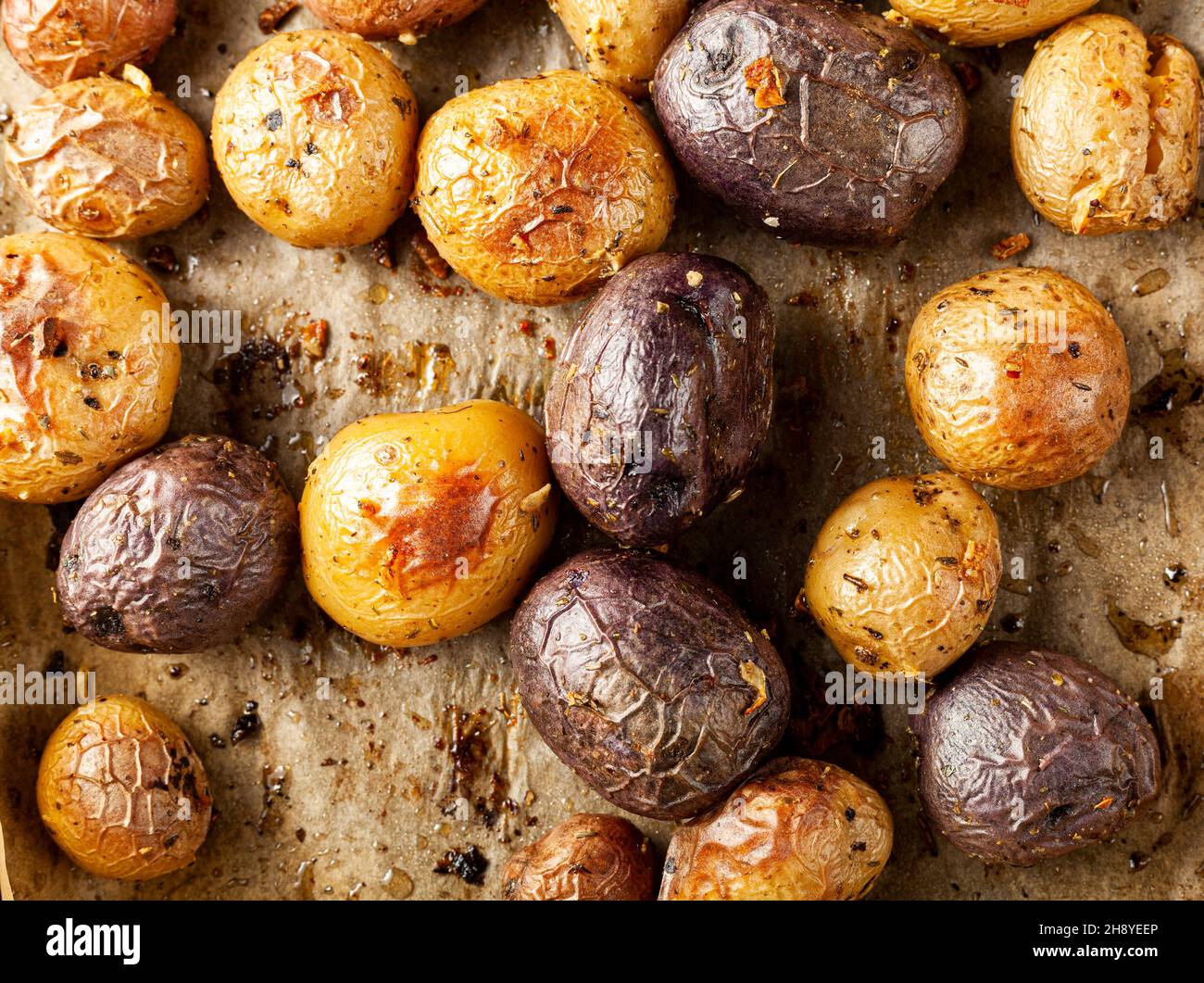 Vista dall'alto immagine ravvicinata che mostra un medley di patate appena sfornate al forno con una varietà che include patate a cuore viola. Le patate si raffreddano sulla carta da forno. C Foto Stock