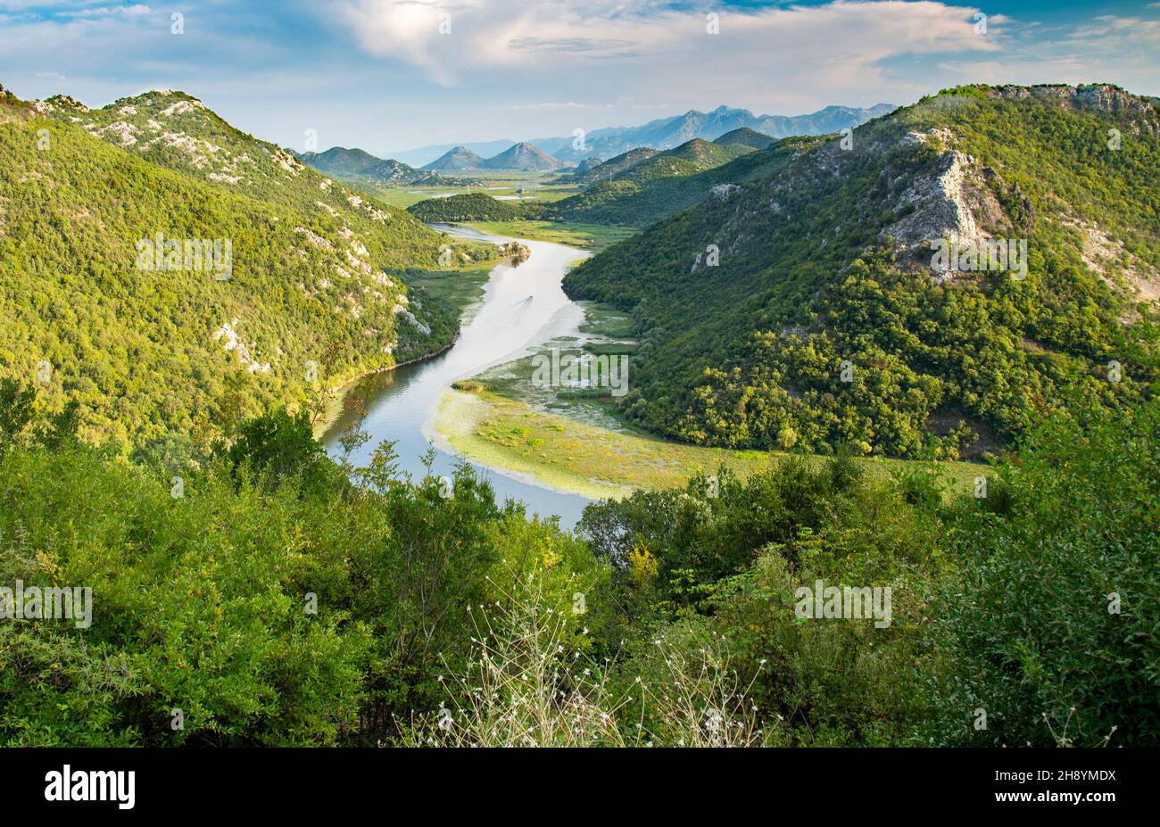 Vista dal punto di vista di Pavlova Strana di una piccola barca che naviga lungo la curva a ferro di cavallo che si snoda intorno alle montagne, e le montagne albanesi in distan Foto Stock