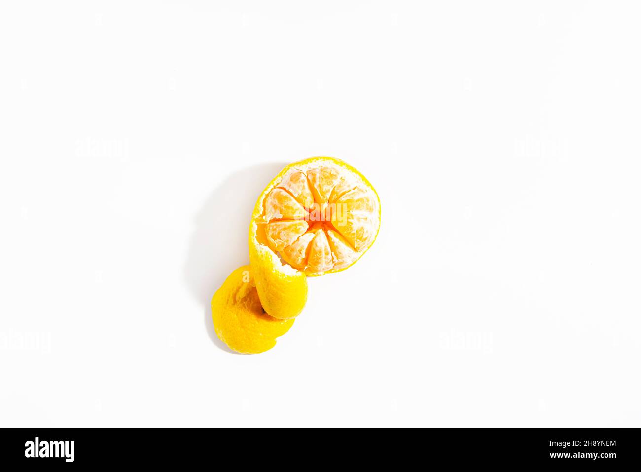 La metà pelata di mandarino con una buccia a forma di spirale giace su uno sfondo bianco. Isolare. Stile di vita. Primo piano. Vista dall'alto. Foto orizzontale. Foto di alta qualità Foto Stock
