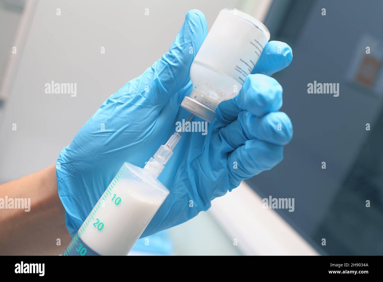 Medico di sesso maschile nei guanti blu che riempiono la siringa con il farmaco bianco per iniezione. Foto Stock