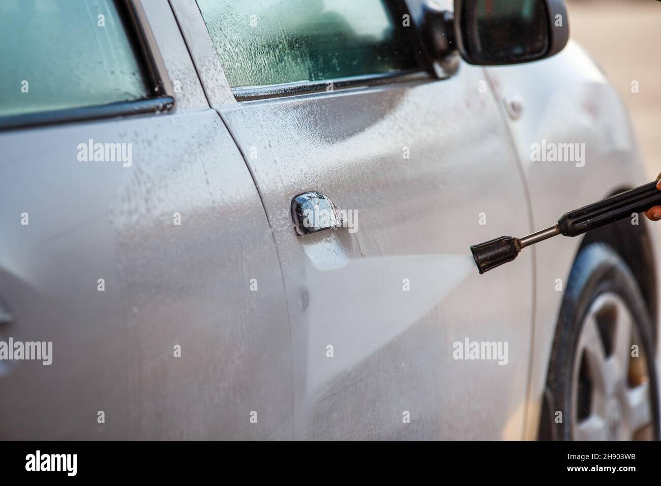 mano con lavatrice ad alta pressione lavaggio auto bianca presso la stazione di lavaggio auto pubblico self-service Foto Stock