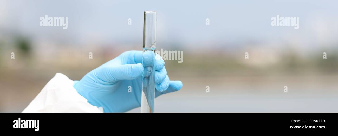 Scienziato in guanti di gomma che tengono una provetta con un campione d'acqua proveniente dalla chiocciatura del fiume Foto Stock