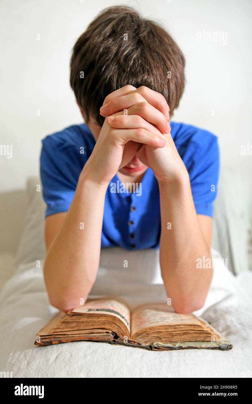 Giovane con una Bibbia che prega sul letto Foto Stock