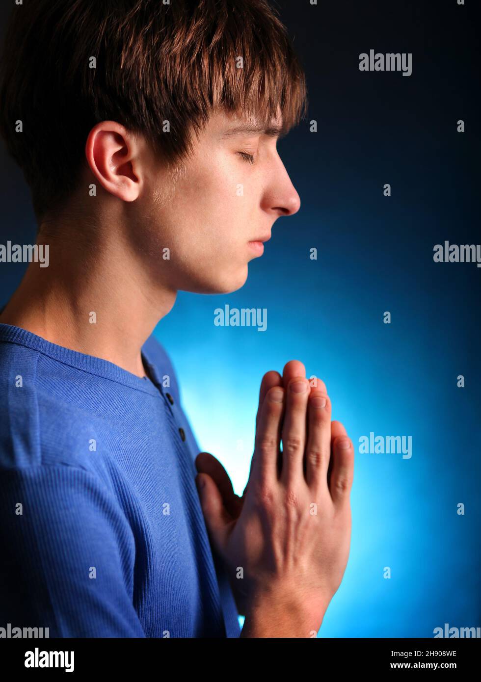 Il giovane che prega nella stanza oscura Foto Stock