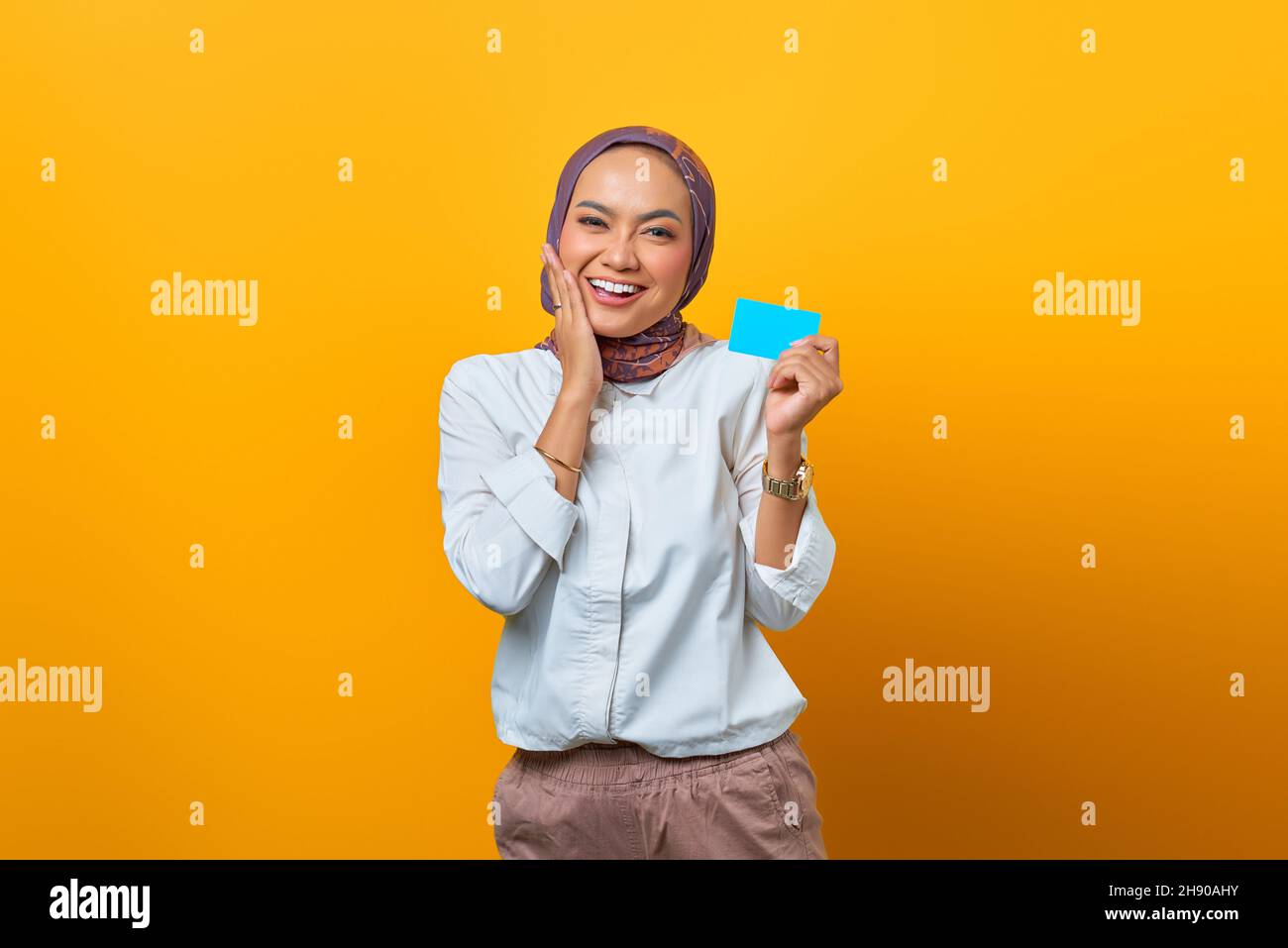 Sorridente donna asiatica tenendo carta bianca e toccare le guance su sfondo giallo Foto Stock