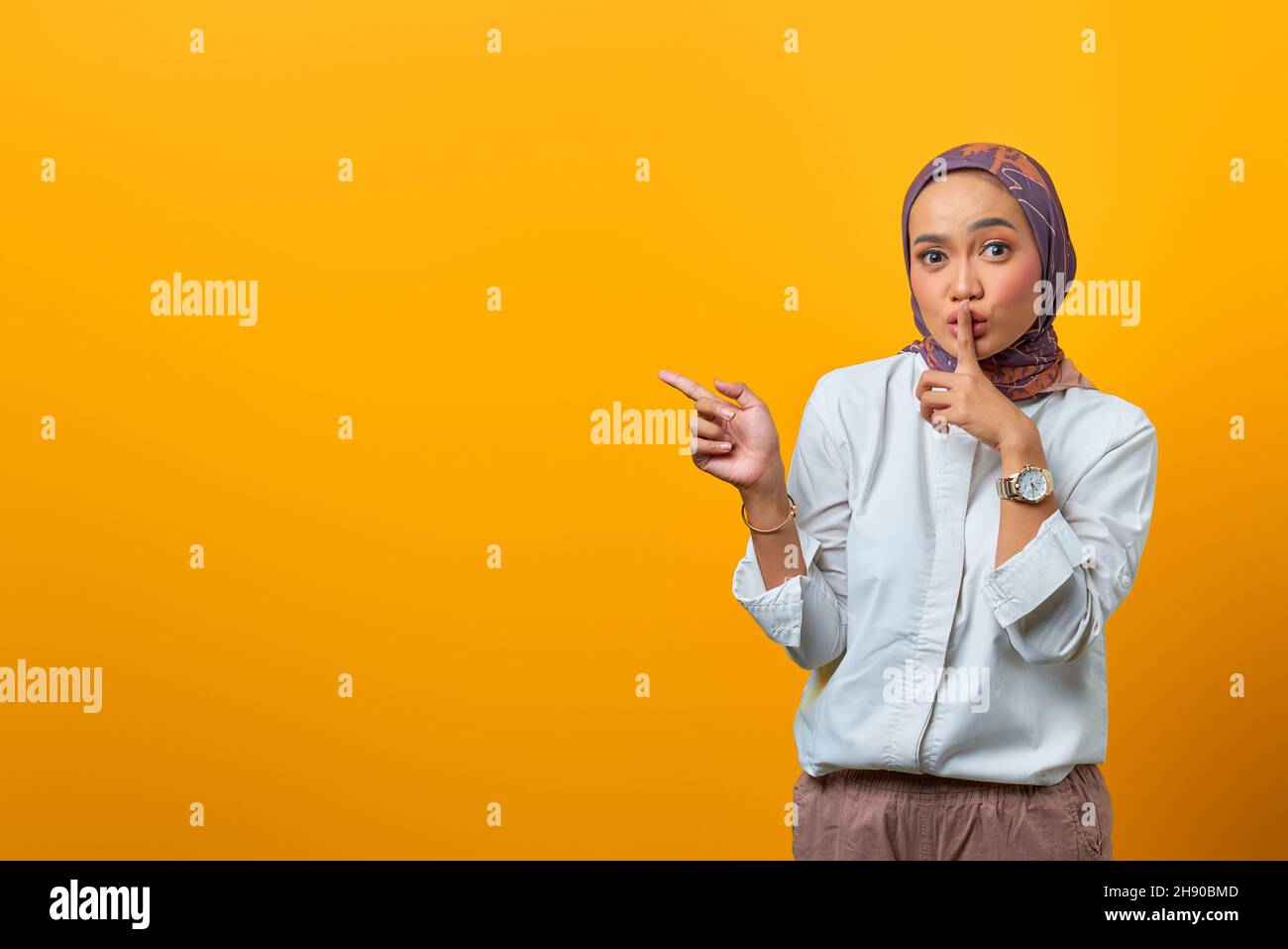 Bella donna asiatica segnale al silenzio e puntando al lato su sfondo giallo Foto Stock