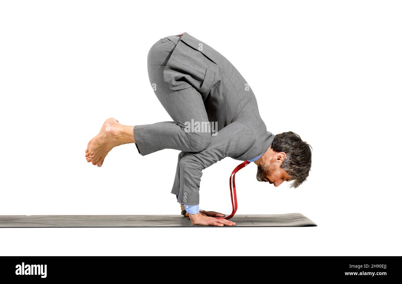 Elegante uomo d'affari a piedi nudi che fa una posa di yoga di corvo equilibrando le sue mani su un tappeto di esercitazione in una vista laterale isolato sopra uno sfondo bianco dello studio Foto Stock