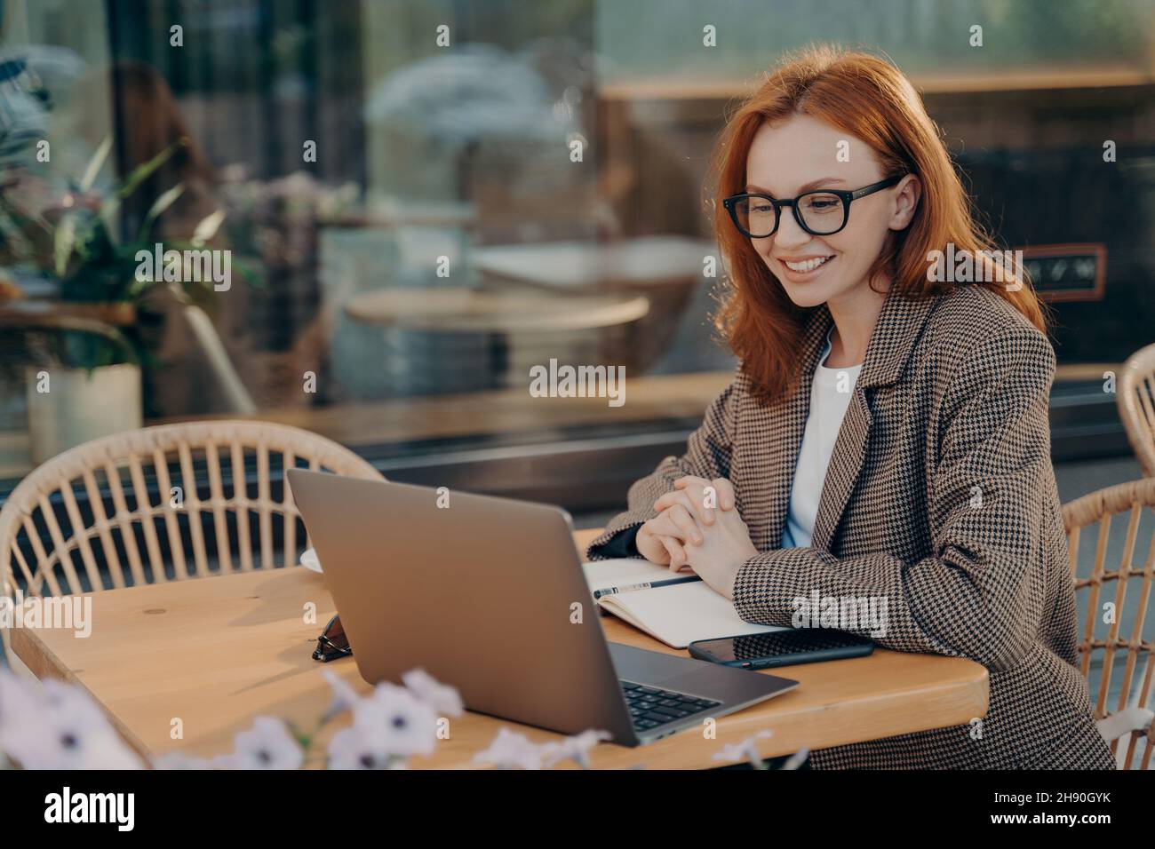 Redhead femmina freelance orologi webinar di formazione fa note in blocco note si siede di fronte al laptop Foto Stock
