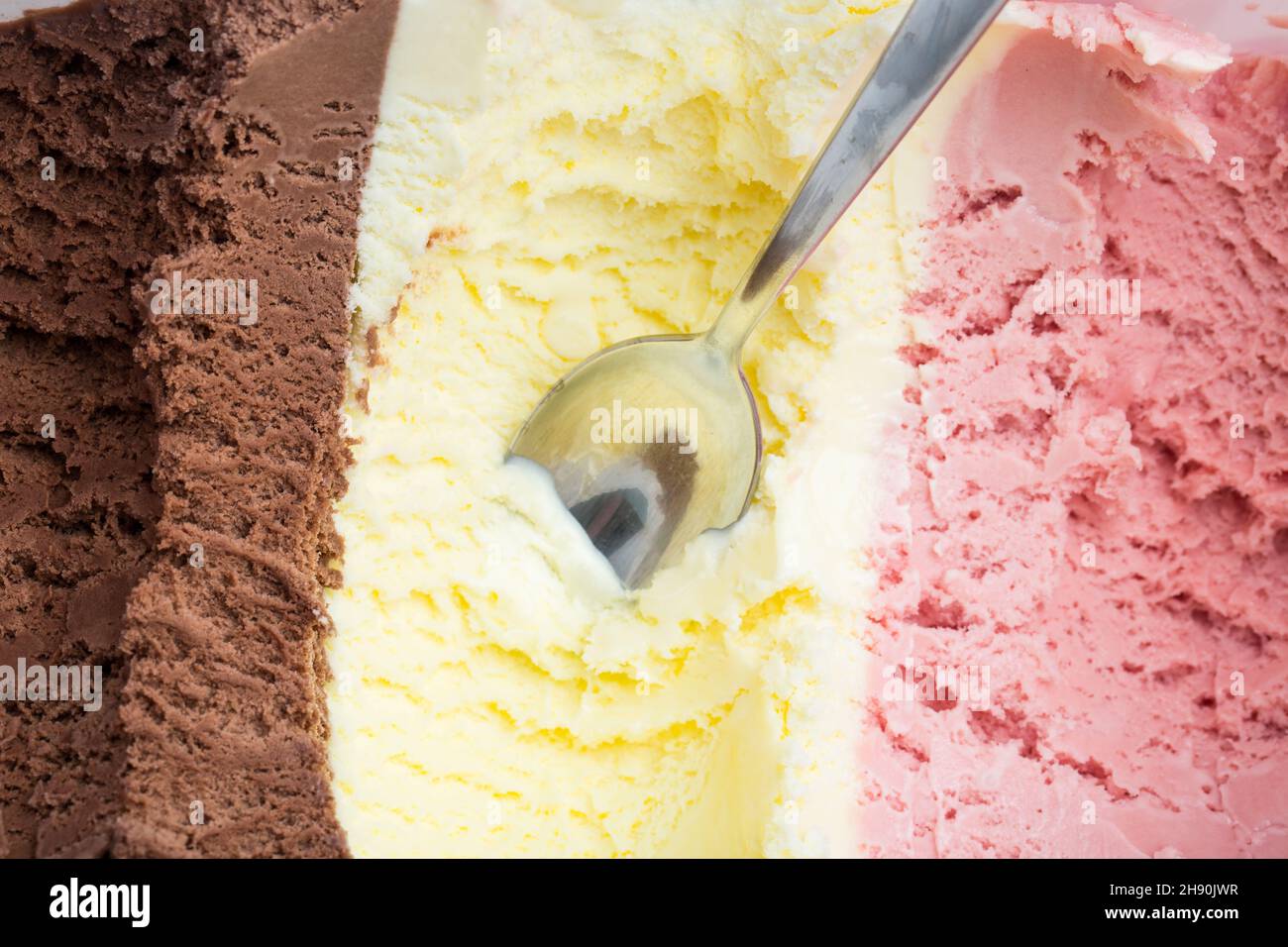 Gelato: Un cucchiaio in una grande scatola di ghiaccio con cioccolato, vaniglia e gelato alla fragola Foto Stock