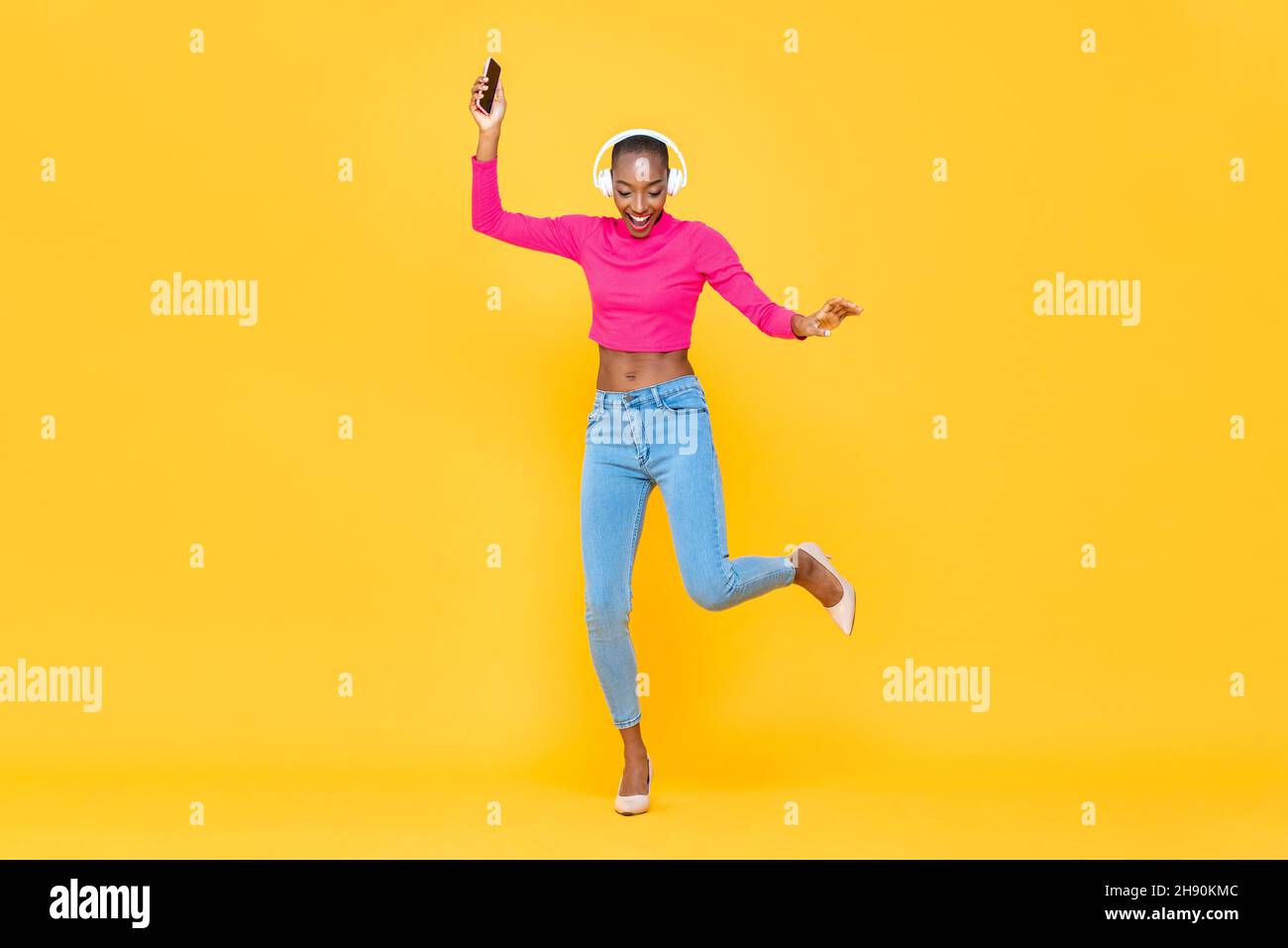Ritratto a tutta lunghezza di donna afro-americana felice che ascolta musica e danza in studio colore giallo sfondo isolato Foto Stock