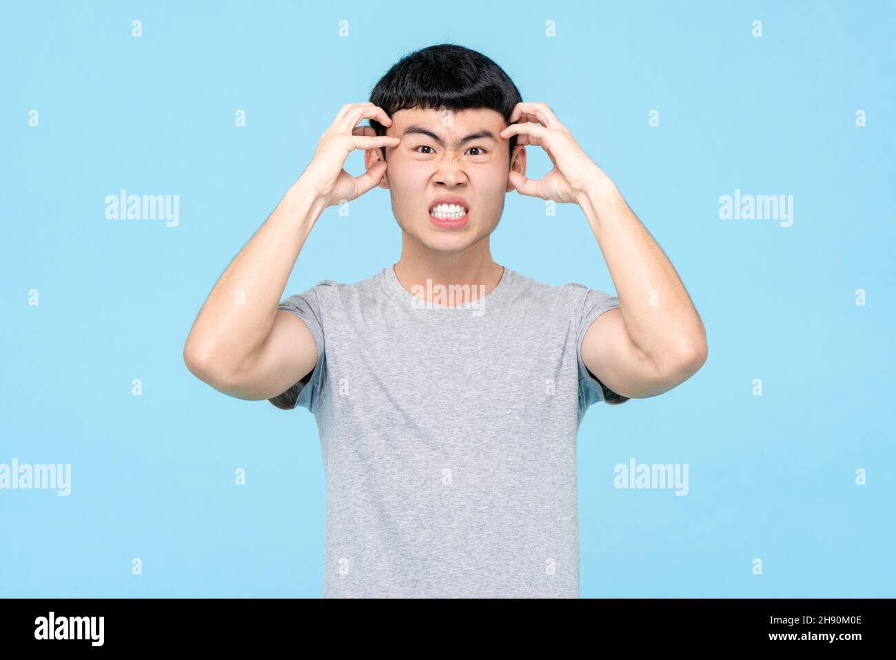 Giovane uomo asiatico che esprime emozione arrabbiata su isolato sfondo azzurro studio Foto Stock