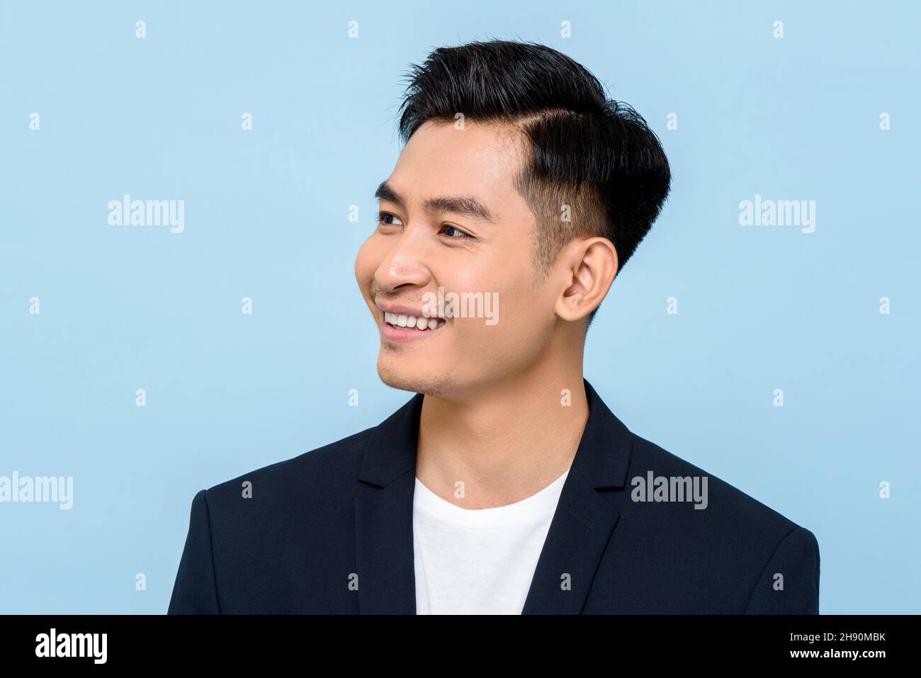 Giovane uomo asiatico sorridente e guardando lateralmente in isolato colore blu chiaro sfondo Foto Stock
