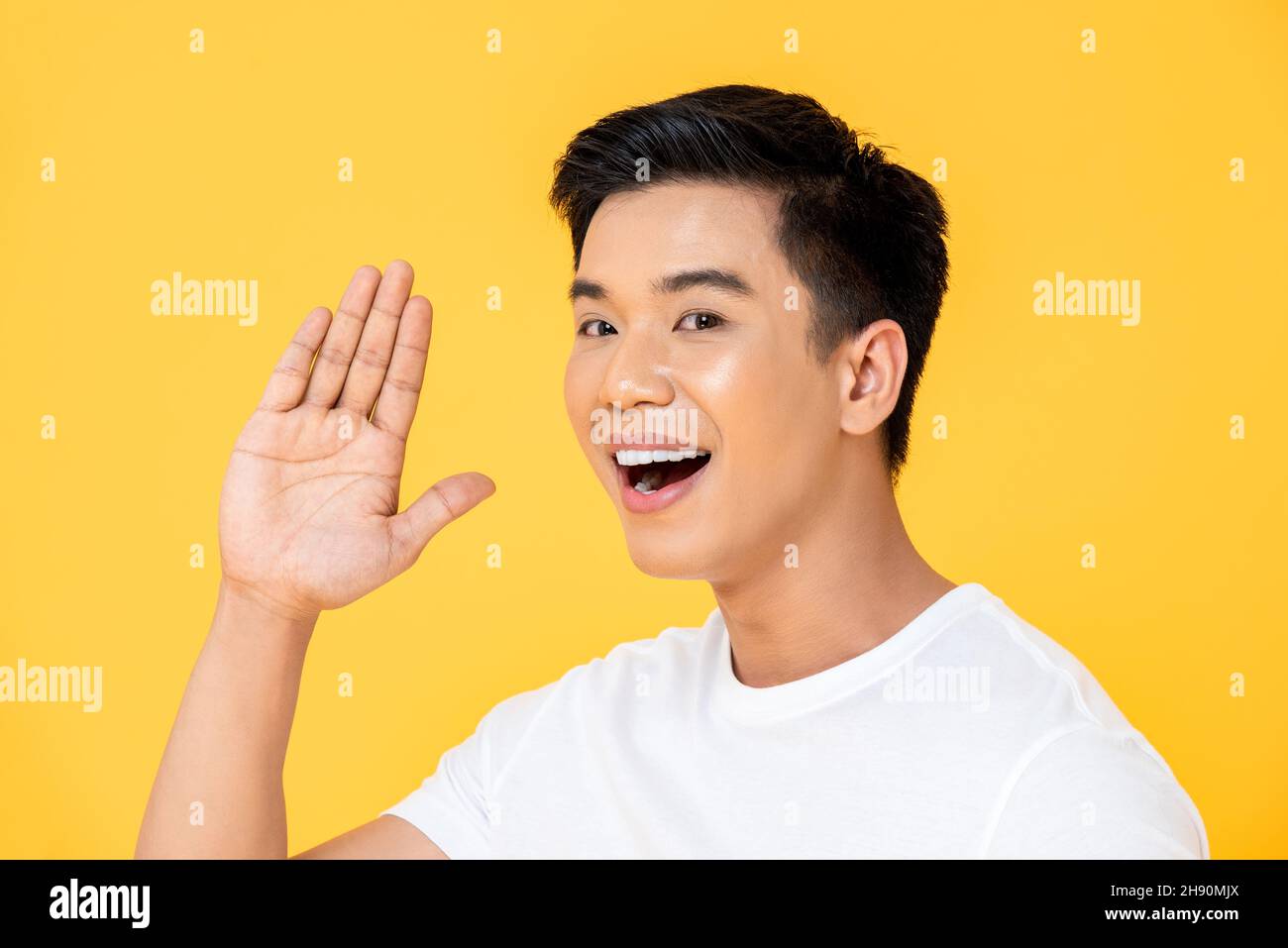 Giovane bell'uomo asiatico che agita la mano e che dice ciao in isolato sfondo giallo studio Foto Stock