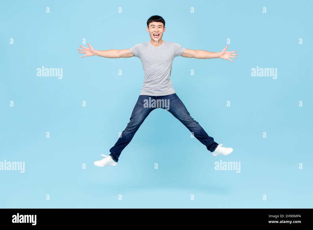 Ritratto a corpo pieno di giovane allegro e vivace uomo asiatico che salta con mani e gambe aperte in studio isolato su sfondo azzurro chiaro Foto Stock