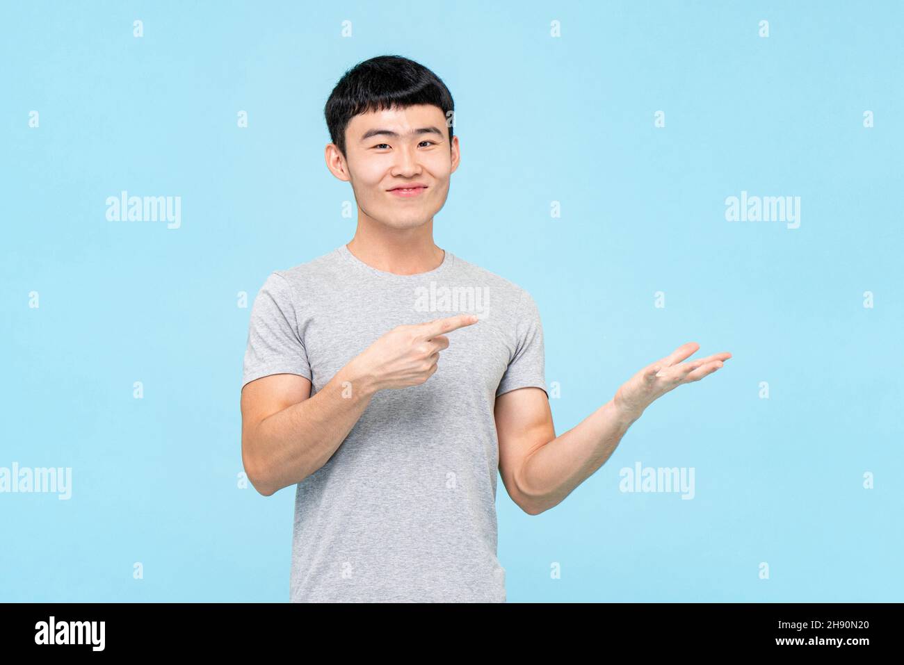 Ritratto del giovane asiatico felice uomo puntando dito ad altra mano vuota aperta in isolato sfondo blu studio per la recomendazione presentare concetto Foto Stock