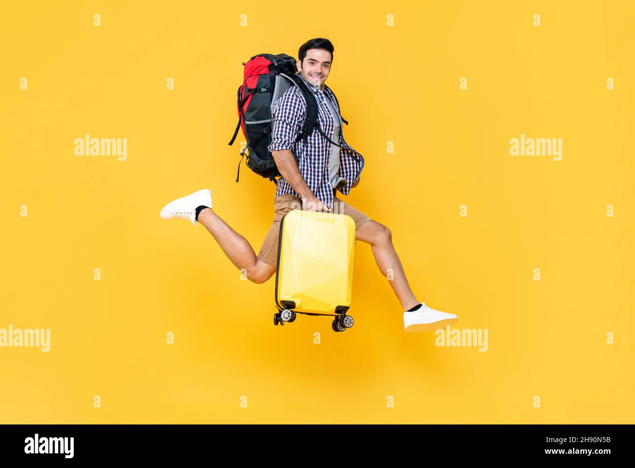 Giovane turista caucasico maschio con il salto di bagagli a mezz'aria pronto per viaggiare isolato su sfondo colorato studio giallo Foto Stock