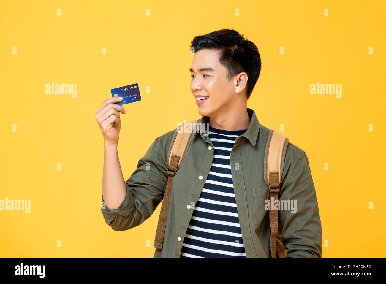 Ritratto di viaggio del giovane turista asiatico uomo zaino in spalla cercando carta di credito in mano isolato su sfondo giallo Foto Stock
