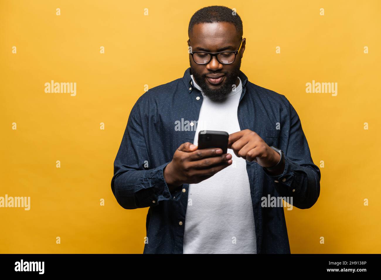 Foto di attraente uomo nero con bearded in una camicia casual utilizzando smartphone isolato su sfondo grigio, tocca lo schermo del telefono, strumento necessario per la produttività, trova ispirazione online Foto Stock