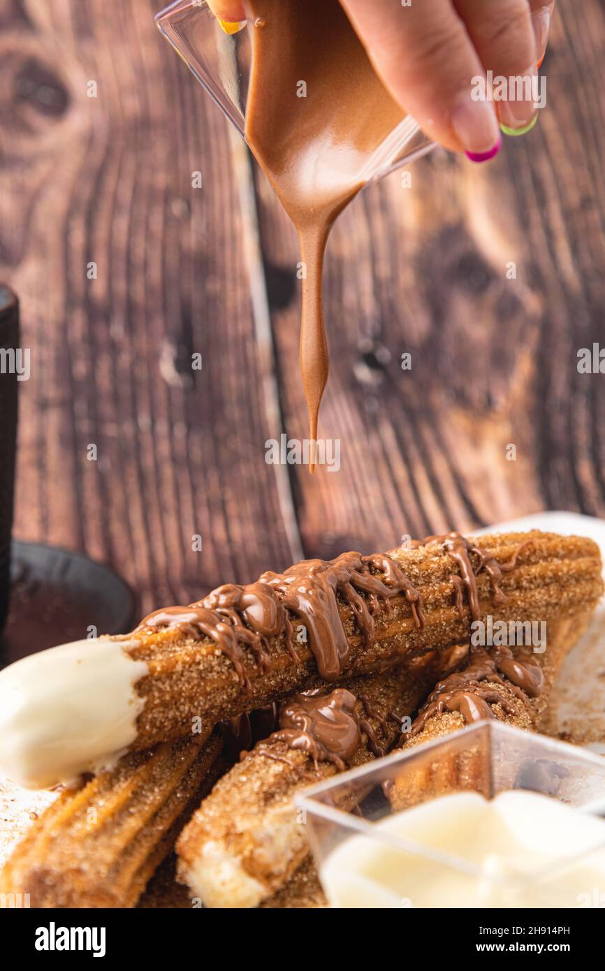Churros caldi con salsa di cioccolato su tavola di legno. Foto Stock