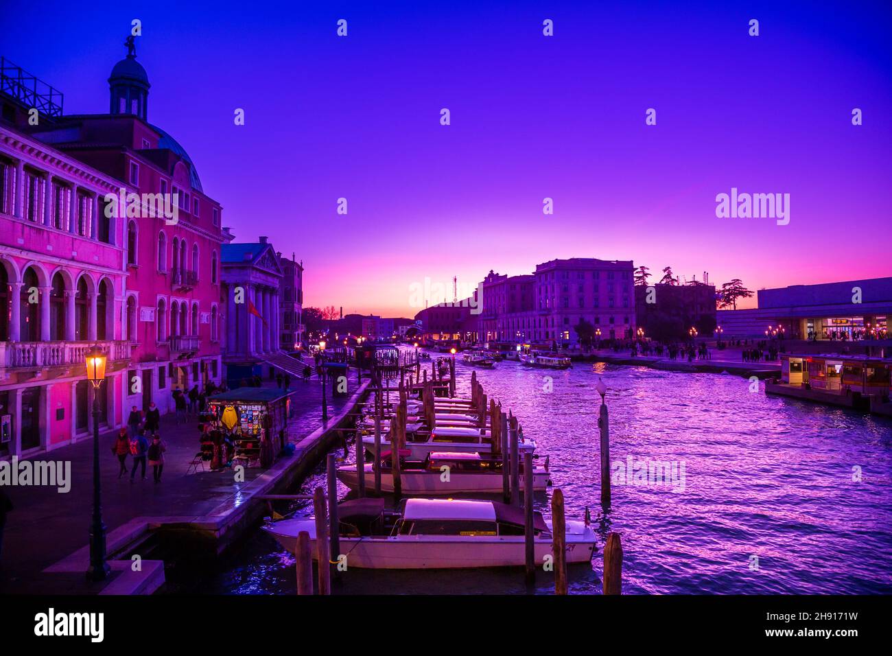 Bellissimo scatto del paesaggio urbano di Venezia con barche su un canale sotto un cielo viola al tramonto Foto Stock