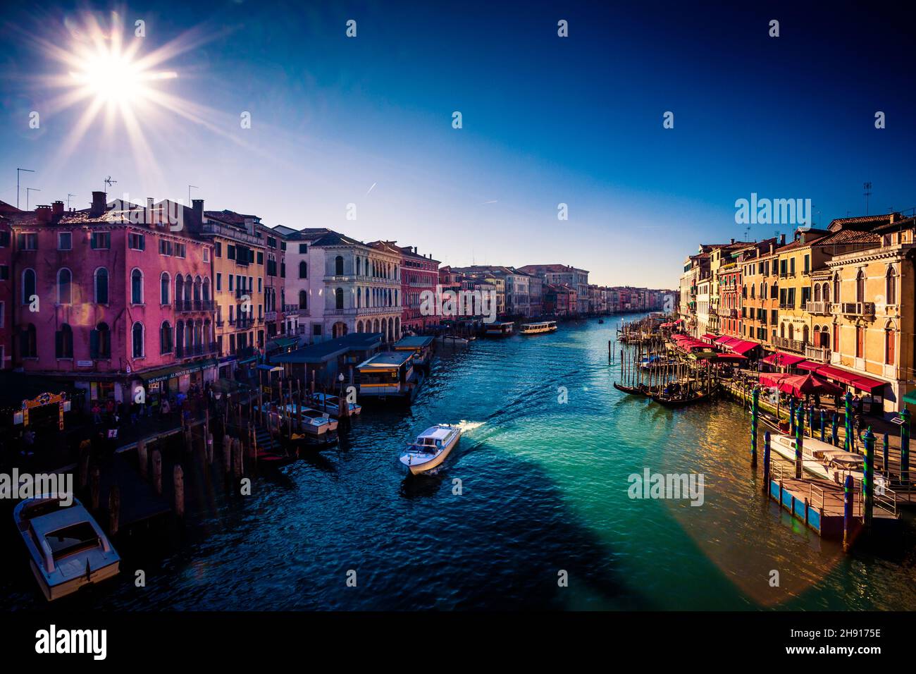 Bellissimo scatto del paesaggio urbano di Venezia con barche su un canale sotto un cielo blu in una giornata di sole Foto Stock