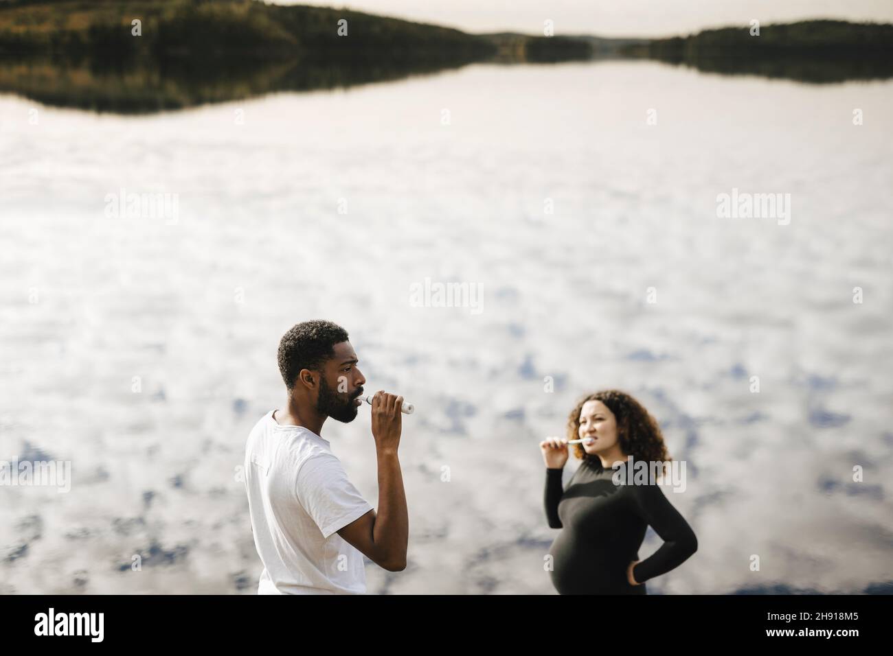 Giovane donna incinta spazzolando i denti con il ragazzo al mattino contro il lago Foto Stock