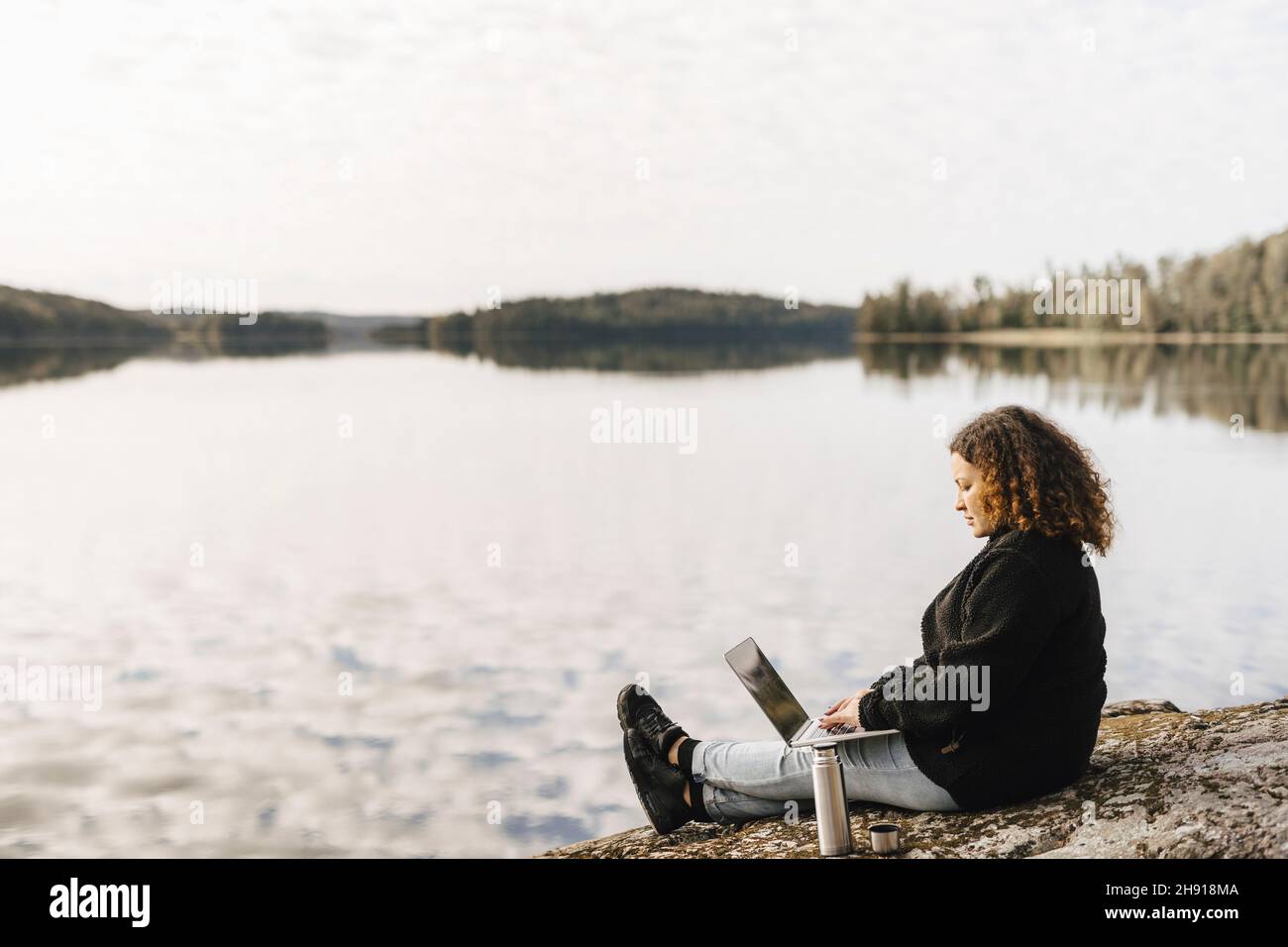 Donna che lavora su un notebook in remoto a Lakeshore durante il fine settimana Foto Stock