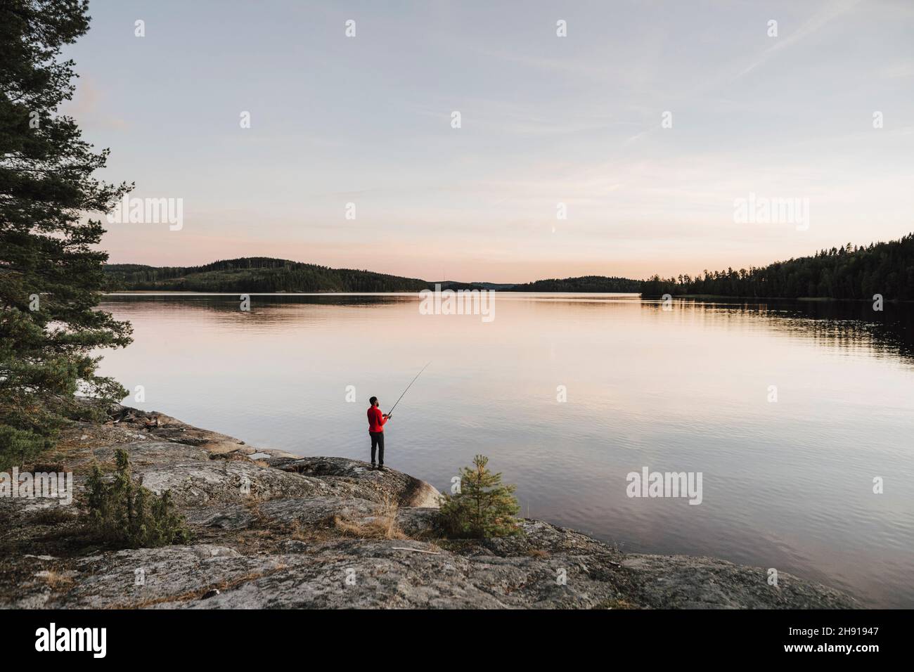 Tutta la lunghezza dell'uomo che pesca al lago durante il tramonto Foto Stock