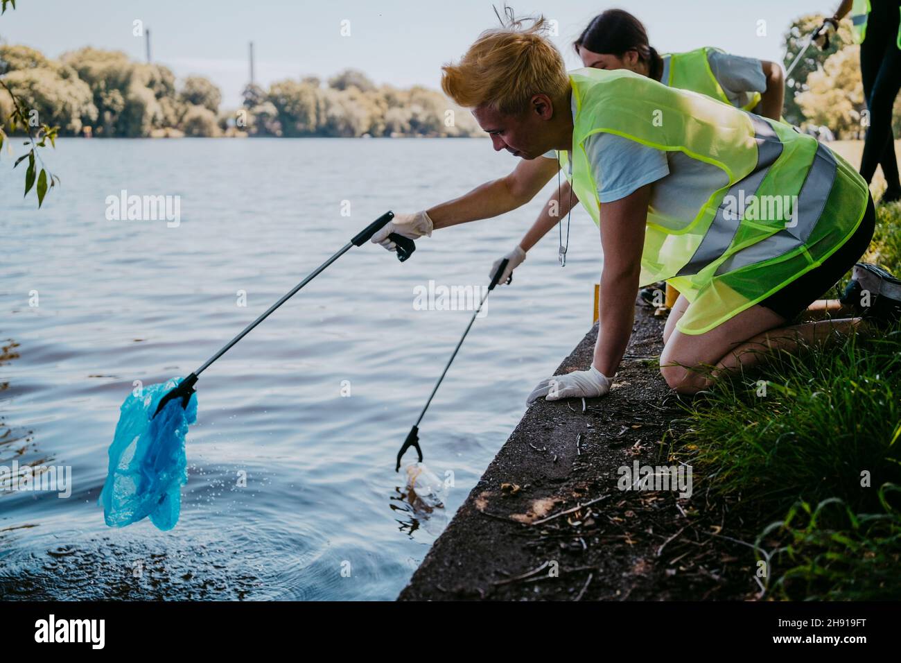 Ambientalisti maschili e femminili che raccolgono materie plastiche con artigli dal lago Foto Stock