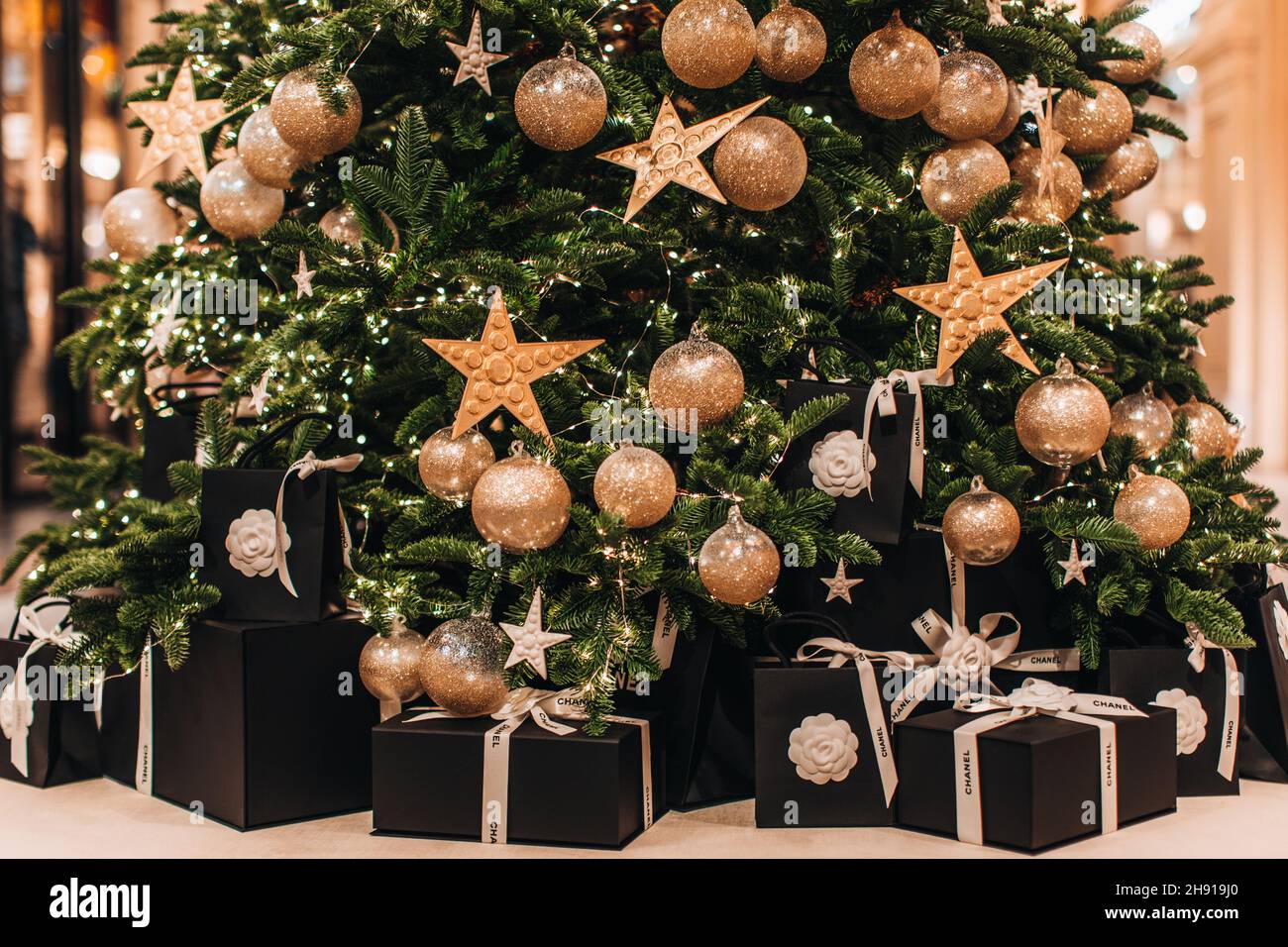 Scatole nere regalo festive con nastri Chanel bianchi sotto l'albero di Natale con stelle e palle dorate Foto Stock
