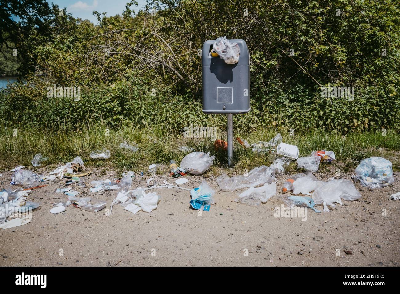 Cestino spazzatura cosparse con rifiuti di plastica intorno in parco Foto Stock