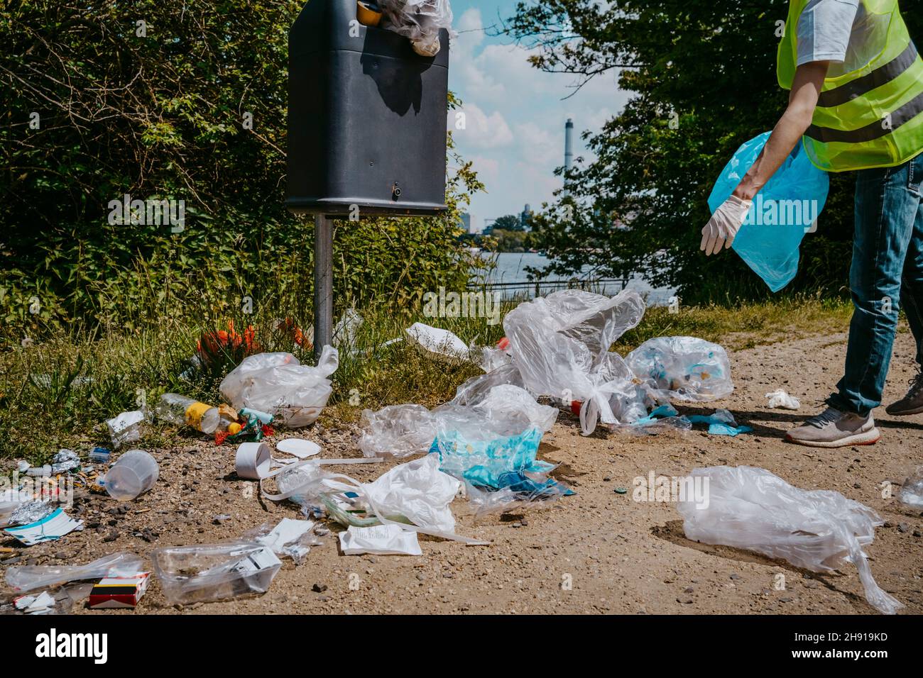 Sezione bassa del volontario maschio che raccoglie i rifiuti di plastica nel cestino dei rifiuti Foto Stock