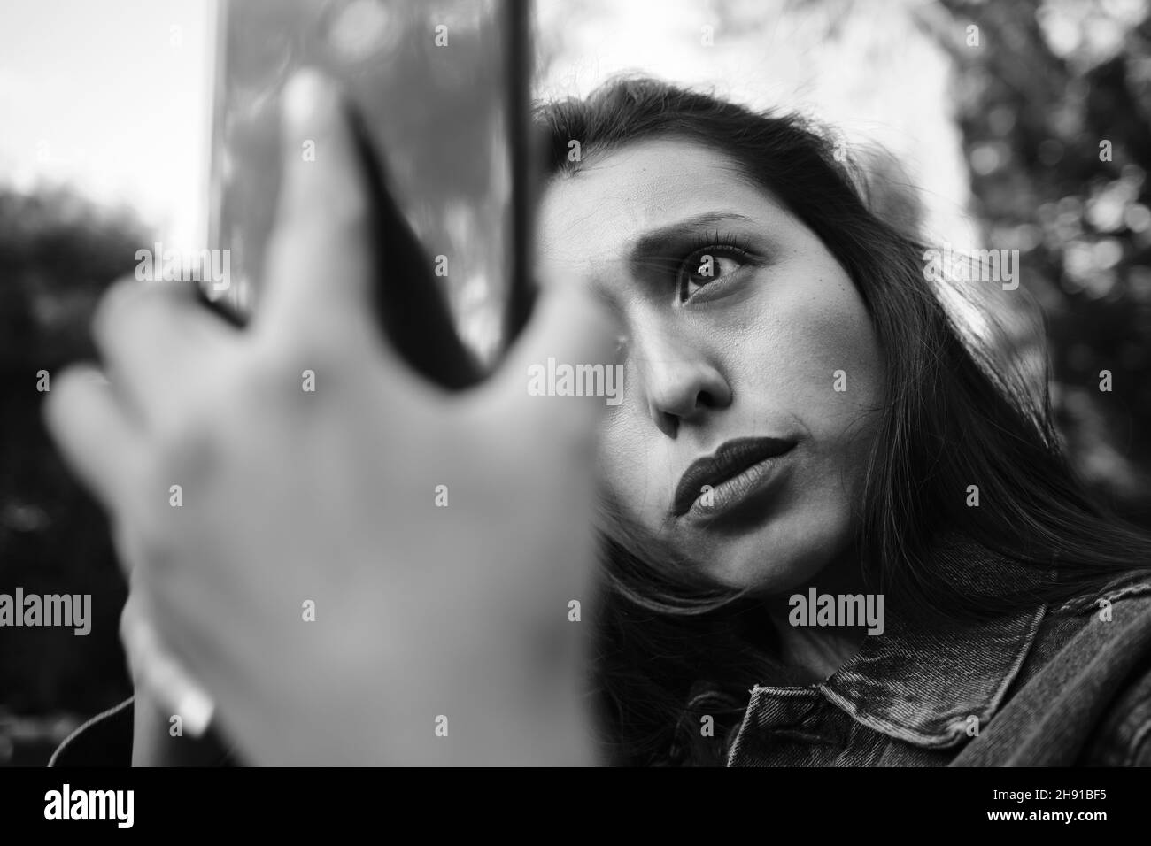 Donna attraente che controlla i suoi capelli nello schermo del suo telefono. Foto Stock