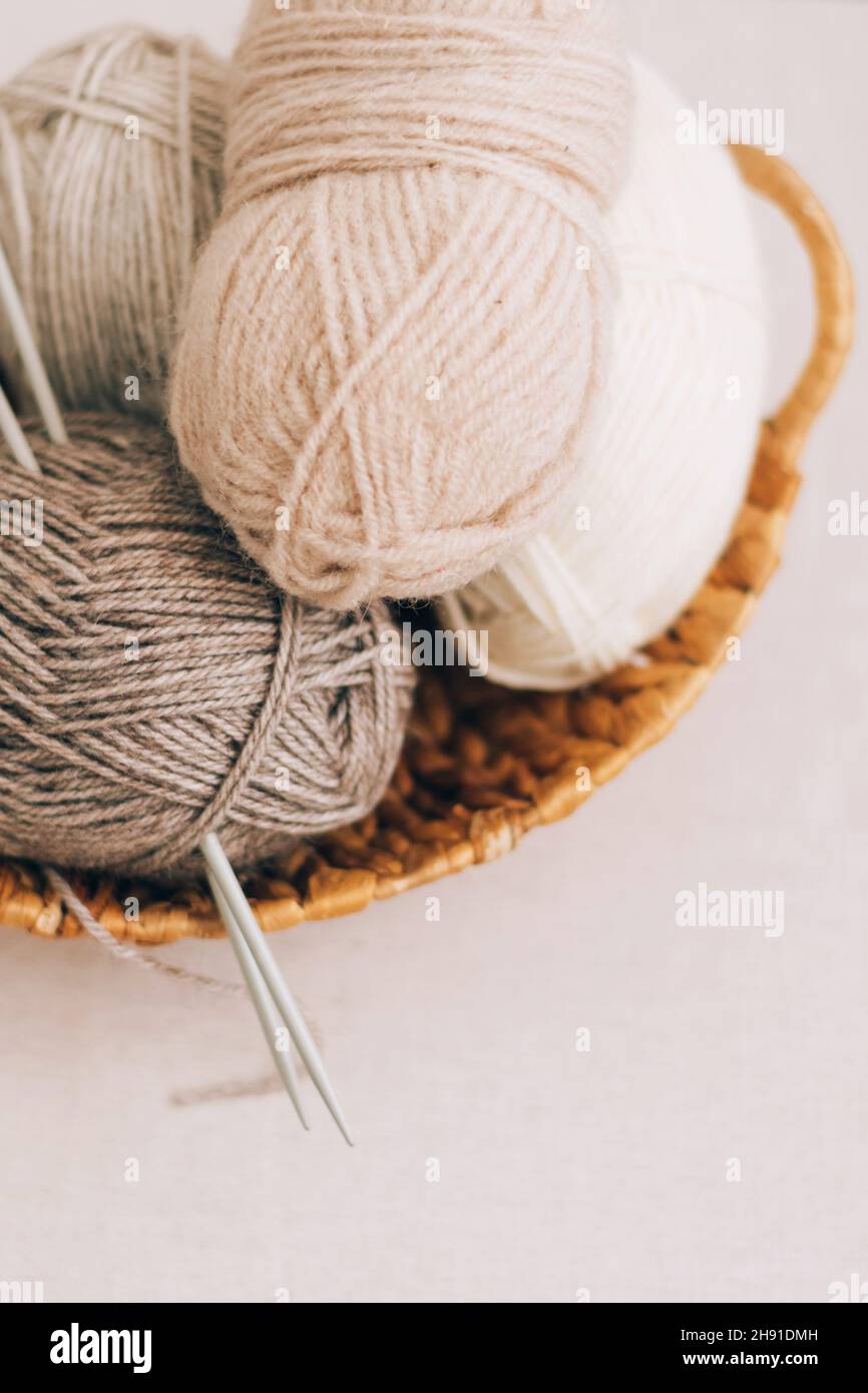 Lana naturale in palle di vari colori pastello in un cestino di vimini. I thread di Unione si avvicinano su uno sfondo chiaro. Foto Stock