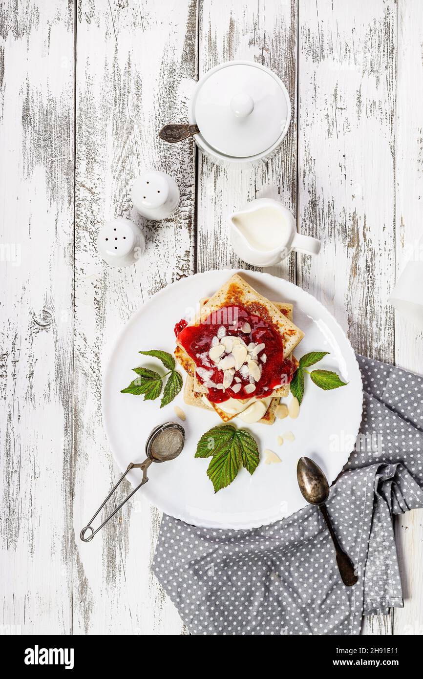 Frittelle tradizionali e deliziose con marmellata di fragole. Colazione gustosa. Pancake fatti in casa con marmellata su sfondo bianco rustico. Servizio di stoviglie bianche. Foto Stock