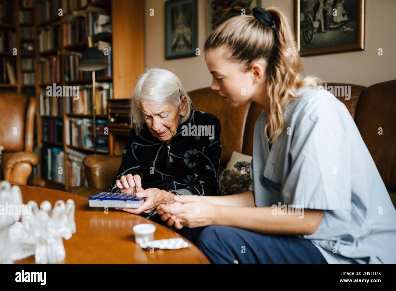 Donna anziana che parla con l'assistente femminile sopra la scatola di medicina nel soggiorno Foto Stock