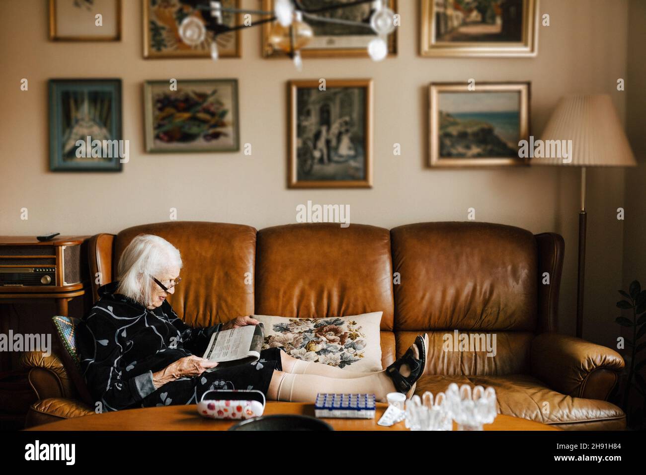 Donna anziana che legge il giornale mentre si siede sul divano nel soggiorno Foto Stock