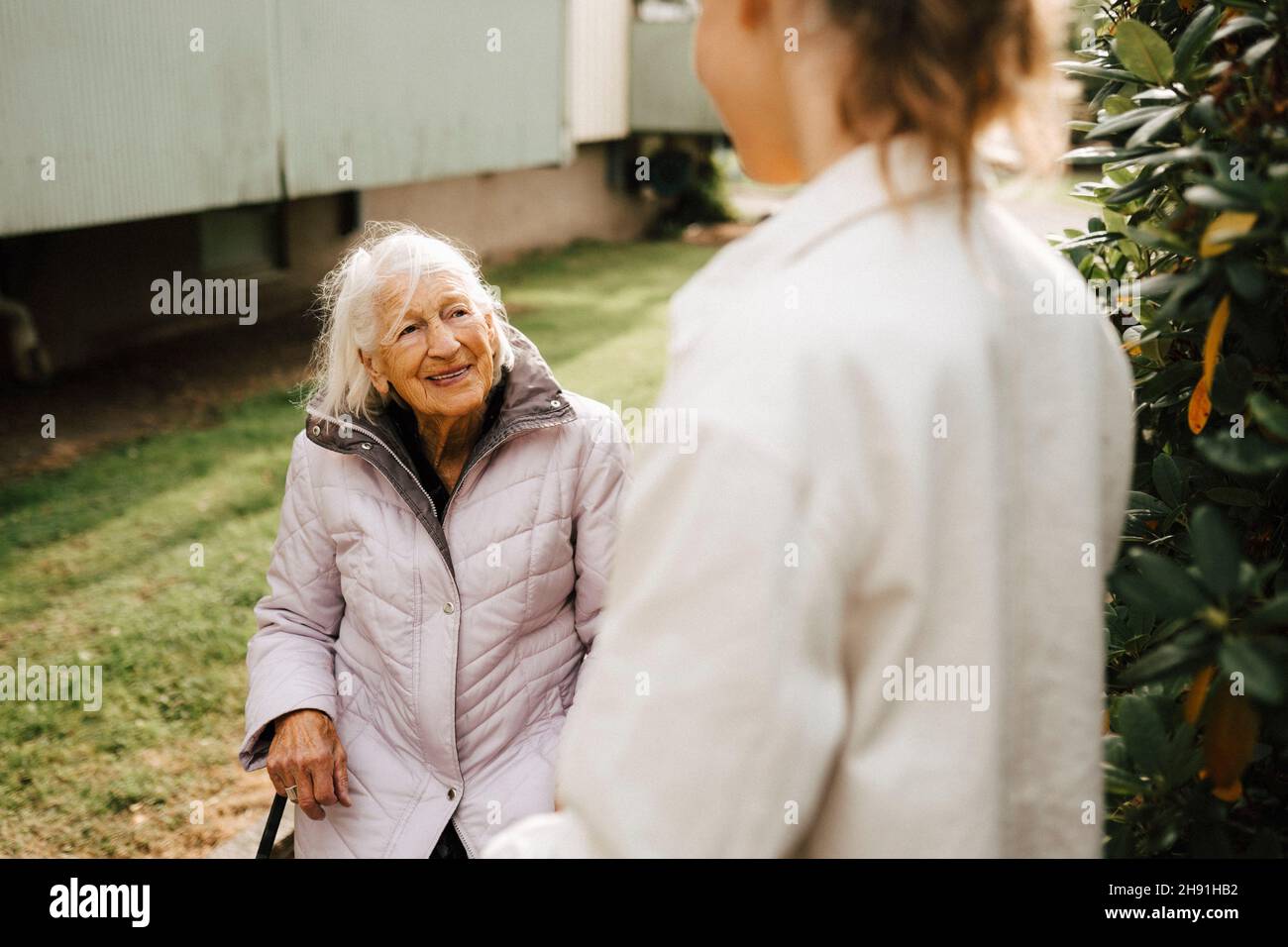 Donna anziana sorridente che parla con l'operatore sanitario di fronte al cortile Foto Stock